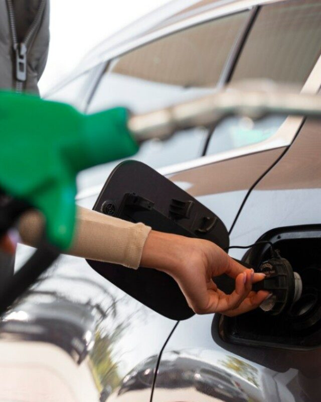 Mano sosteniendo una boquilla verde de diésel llenando el tanque de un auto gris