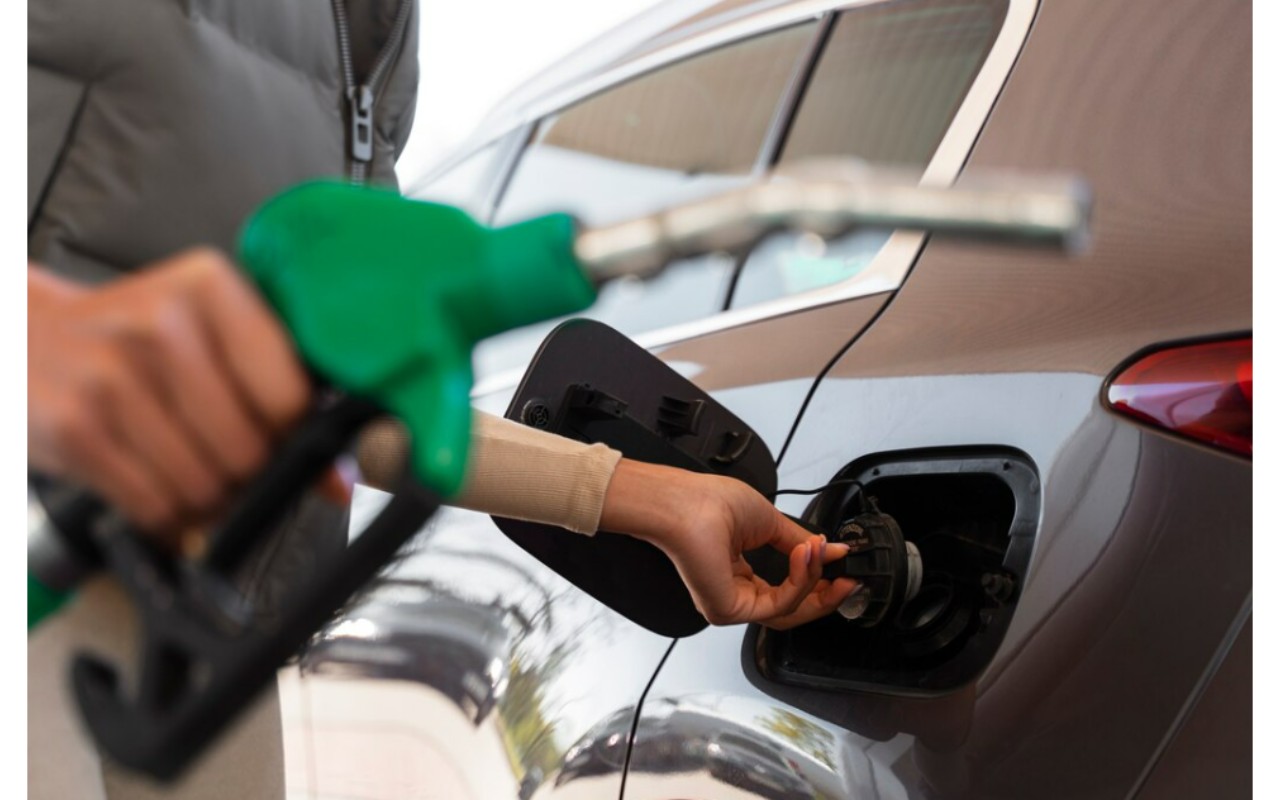 Mano sosteniendo una boquilla verde de diésel llenando el tanque de un auto gris